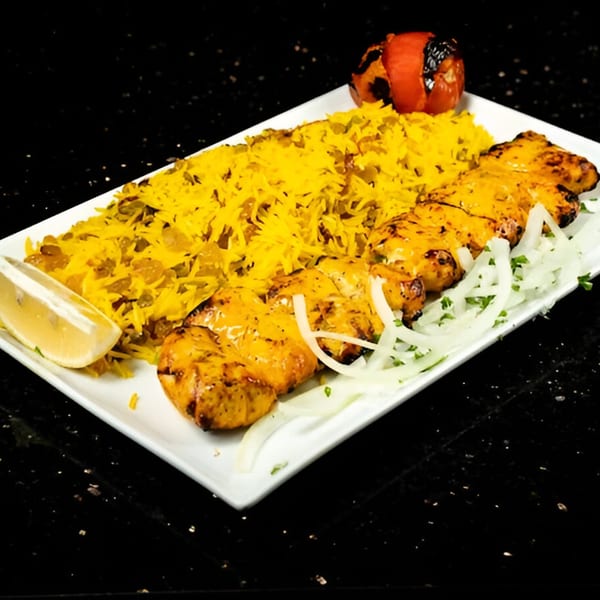 Persian chicken kebab with yellow rice, grilled tomato, and sliced onions on a white plate.