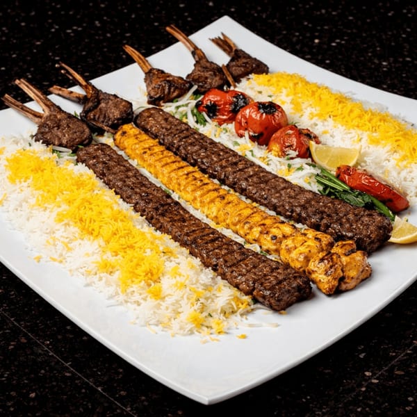 A large platter of Persian kebabs, including lamb chops, koobideh, and chicken, served with rice and grilled tomatoes.