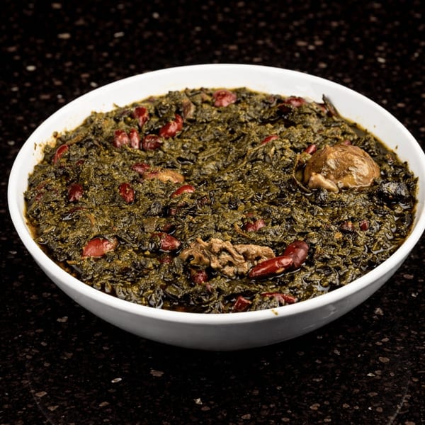 A white bowl filled with Ghormeh Sabzi, a Persian herb stew with red beans and meat.