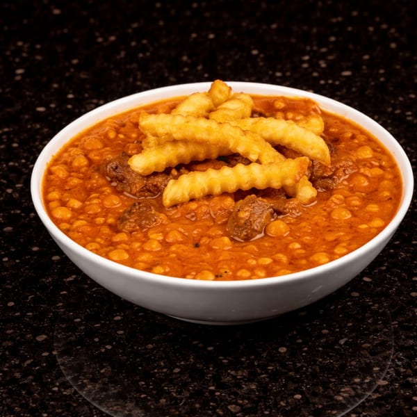 A white bowl of Persian Ghormeh Sabzi stew with meat, beans, and crinkle-cut fries on a dark counter.