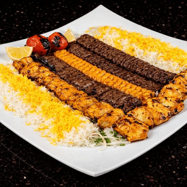 A large platter of Persian kebabs, rice, grilled tomatoes, and lemon wedges.