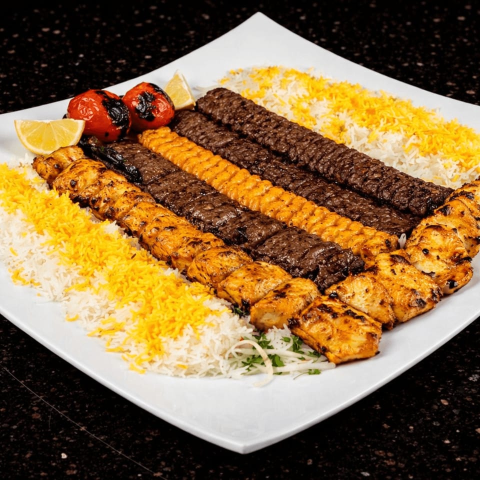 A large platter of Persian kebabs, rice, grilled tomatoes, and lemon wedges.