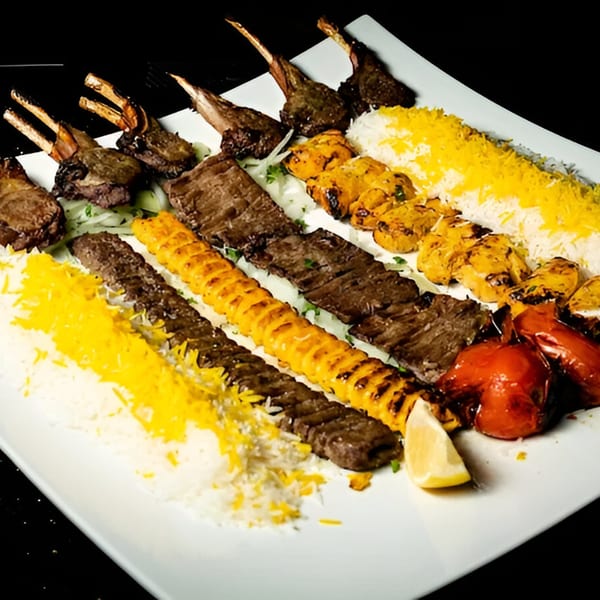 A large platter of Persian kebabs, including lamb chops, koobideh, and chicken, with rice and grilled tomatoes.